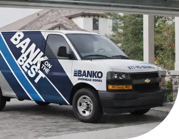 A white and blue Banko Overhead Doors service van is parked in a driveway near a residential garage.