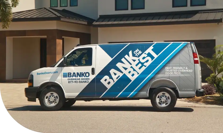 A white and blue Banko Overhead Doors service van is parked in a residential driveway in front of a modern house.