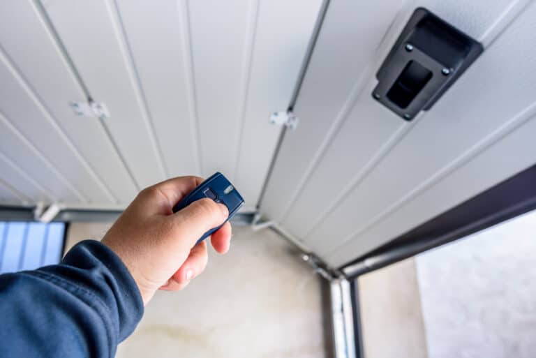 A person’s hand holds a remote control, pointing it toward a partially open garage door from inside the garage.