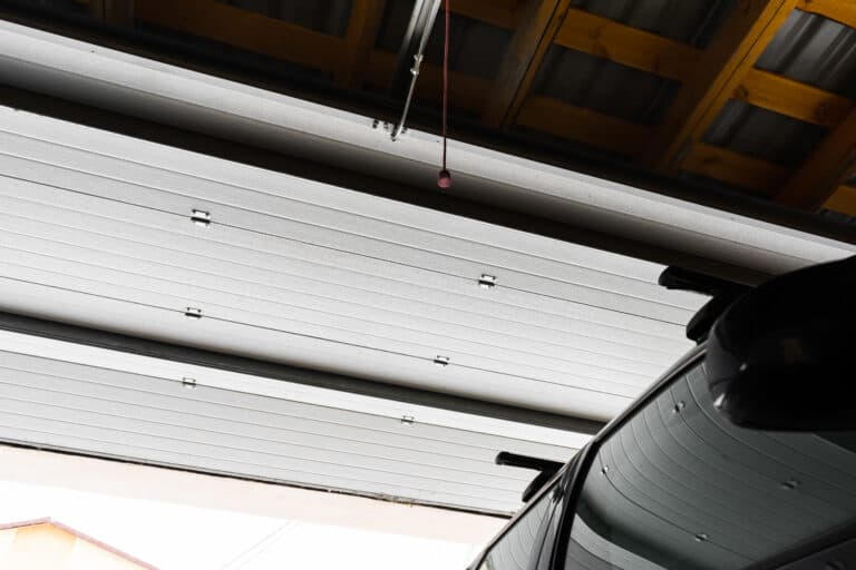 Partially open garage door with a car parked inside, showing the ceiling, door panels, and a red pull cord hanging down.