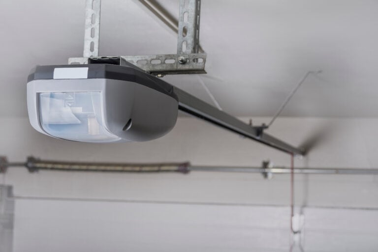 Close-up of a ceiling-mounted garage door opener with a metal rail, installed inside a garage with a white ceiling and walls.